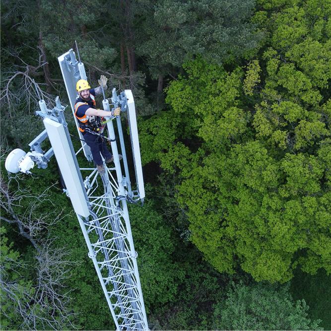 A Mitie engineer wearing safety gear, waving from the top of a telecoms mast